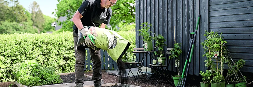 Person füllt Erde in Hochbeet